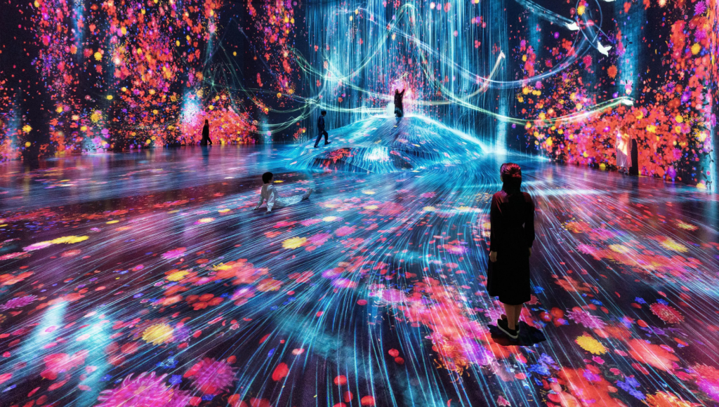 チームラボボーダレス展示ブースの写真。壁床ともにプロジェクションマッピングされていて一面滝をモチーフにしたカラフルなデザイン。奥の床は少し盛り上がっている。人が数人いる。
