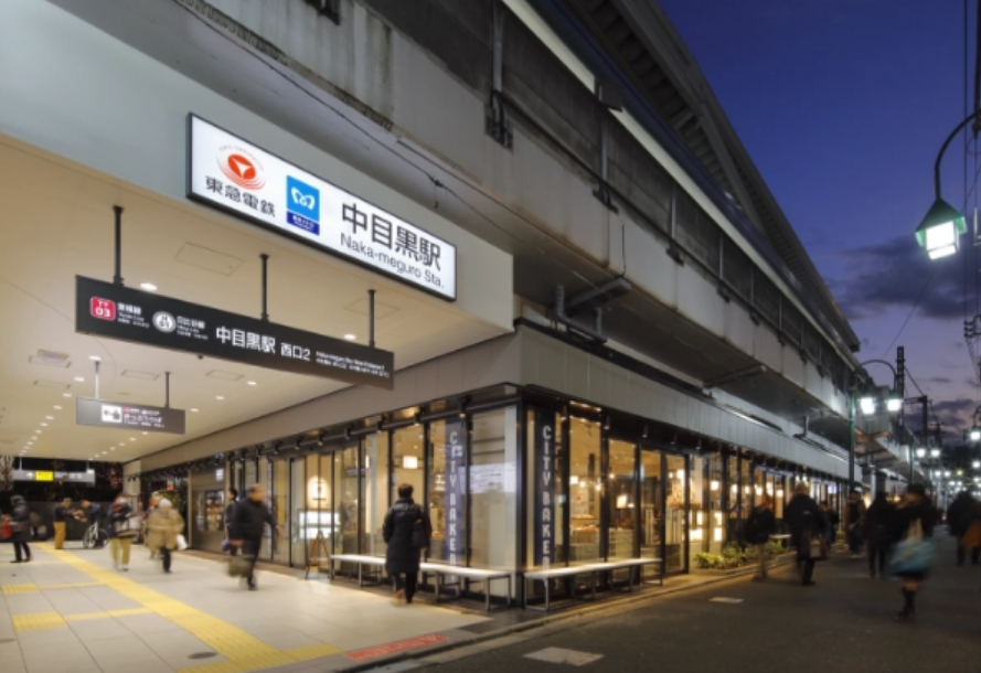 中目黒駅高架下の写真。画像左手前から右奥にかけて道がある。高架下に中目黒駅の看板。その下を多くの人が通っている。