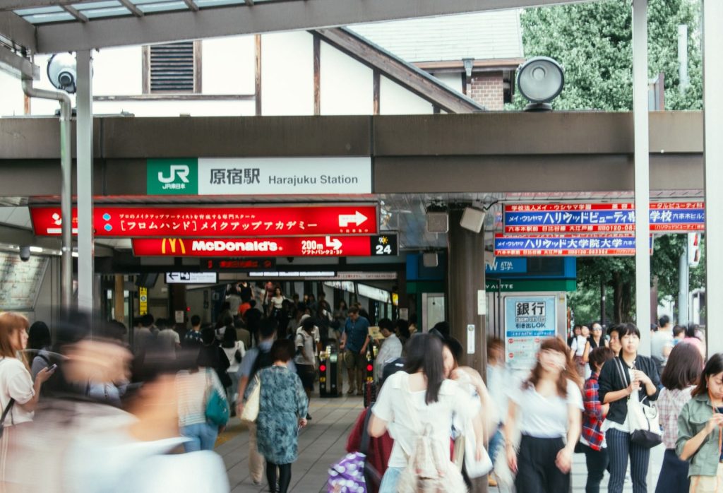 原宿駅の改札を駅舎外から撮影した写真。原宿駅という看板がありその下に改札。多くの人が行き交っている。
