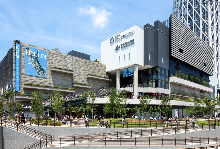 東京ソラマチの写真。右奥には東京スカイツリーの足元が写る。画像全面にソラマチの建物がある。建物前方には広場が広がっていて緑もある。