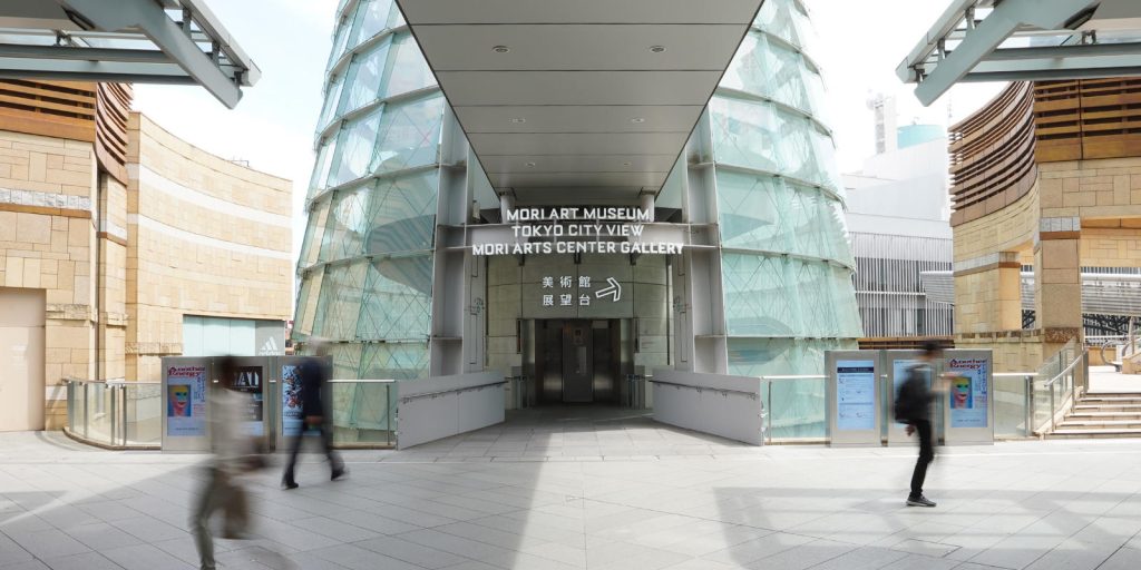 森美術館入口の写真。ガラス張りのドームの中に螺旋階段が続いている。道に面していて左右に道が広がっている。